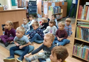 Dzieci siedzą w bibliotece i słuchają czytanego opowiadania.